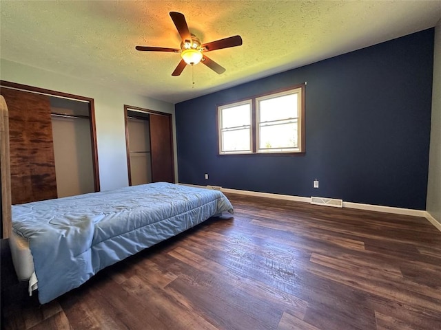 bedroom featuring visible vents, two closets, baseboards, dark wood-style floors, and a textured ceiling