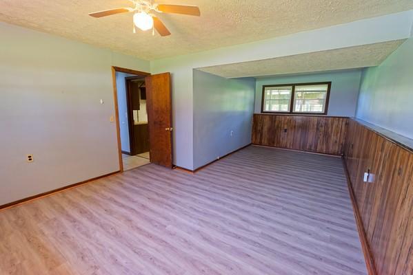 empty room featuring wooden walls, wainscoting, a textured ceiling, a ceiling fan, and wood finished floors