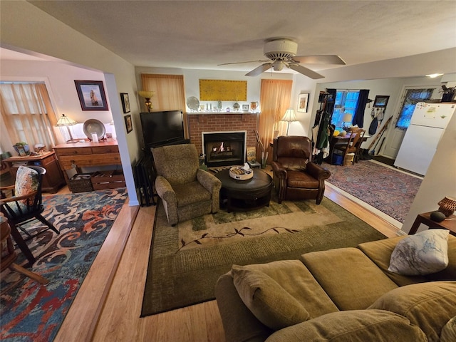 living room with ceiling fan, wood-type flooring, and a brick fireplace