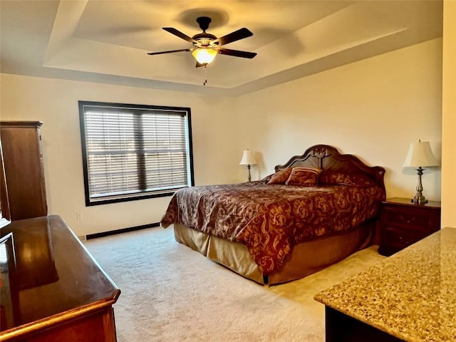 bedroom featuring a tray ceiling, carpet floors, baseboards, and a ceiling fan