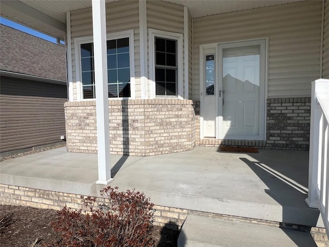 view of exterior entry with brick siding and a porch