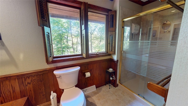 bathroom featuring a shower with door, toilet, plenty of natural light, and wood walls