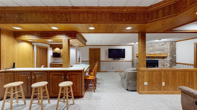 bar featuring light colored carpet, a fireplace, wooden walls, and black microwave