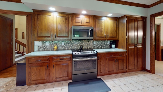 kitchen with light tile patterned floors, stainless steel appliances, tasteful backsplash, and ornamental molding