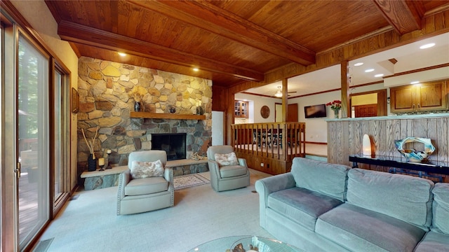 carpeted living room featuring beamed ceiling, a stone fireplace, wood ceiling, and crown molding