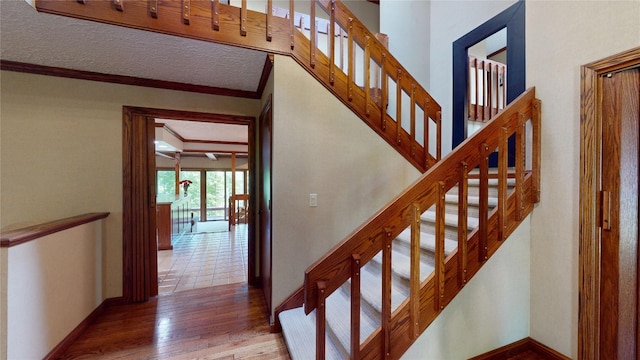 stairs with hardwood / wood-style floors, ornamental molding, and a textured ceiling