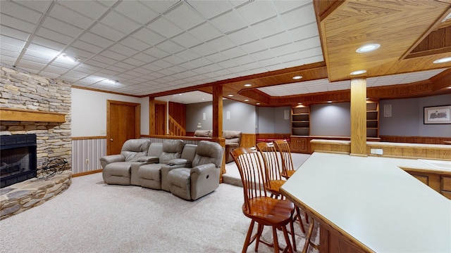 carpeted living room featuring a stone fireplace and crown molding