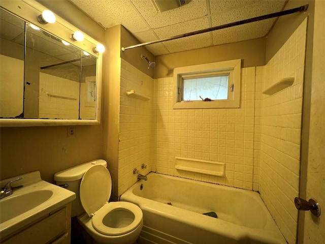 full bathroom with toilet, a drop ceiling, vanity, and tiled shower / bath