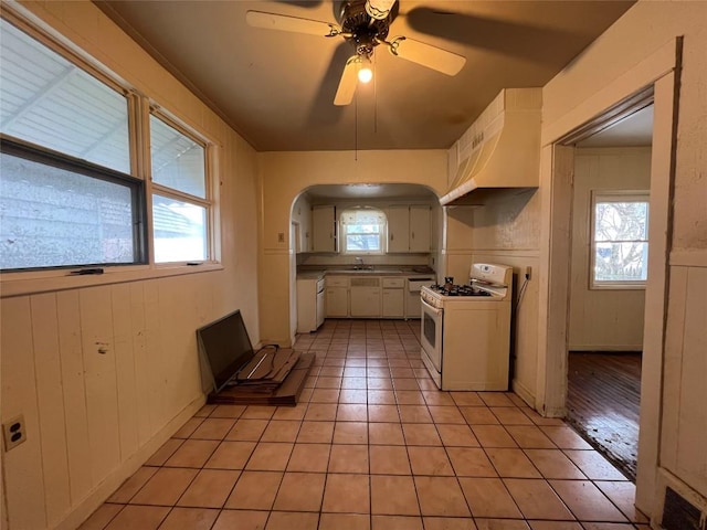 kitchen featuring custom range hood, ceiling fan, light tile patterned floors, white cabinetry, and white gas stove