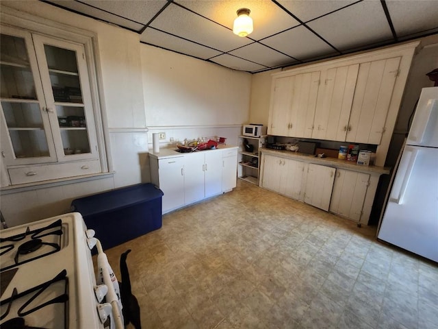 kitchen with white cabinetry, a drop ceiling, and white appliances