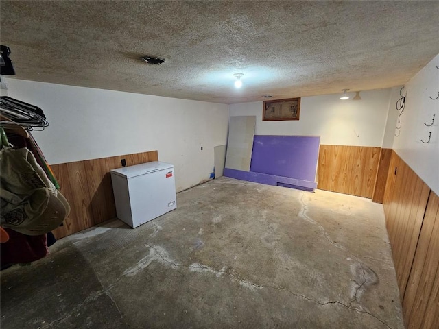 basement with wooden walls, fridge, and a textured ceiling