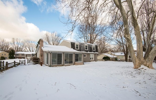 snow covered back of property with a sunroom