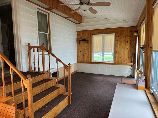 interior space with carpet, wood walls, ceiling fan, and lofted ceiling