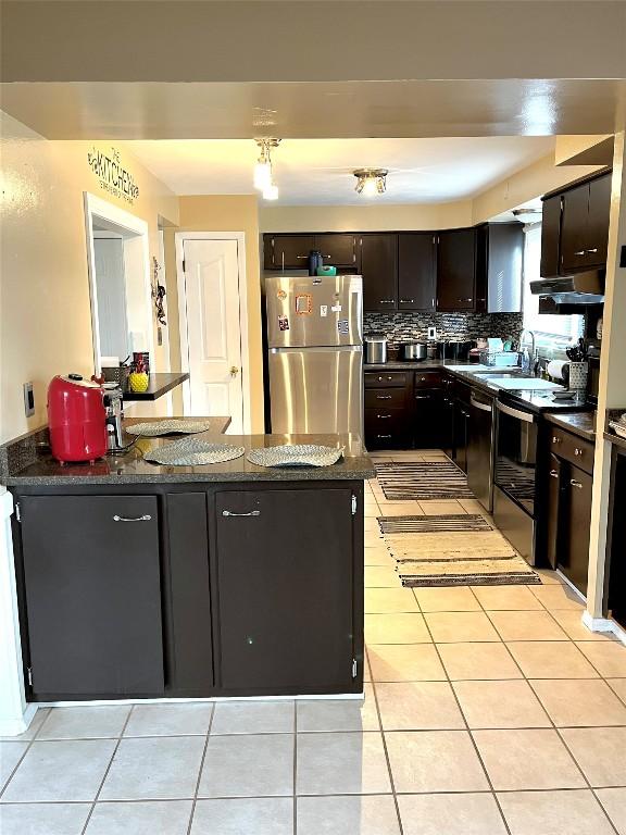 kitchen with dark stone counters, sink, decorative backsplash, light tile patterned floors, and appliances with stainless steel finishes