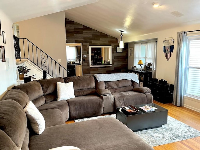 living room featuring wooden walls, sink, light hardwood / wood-style floors, and lofted ceiling