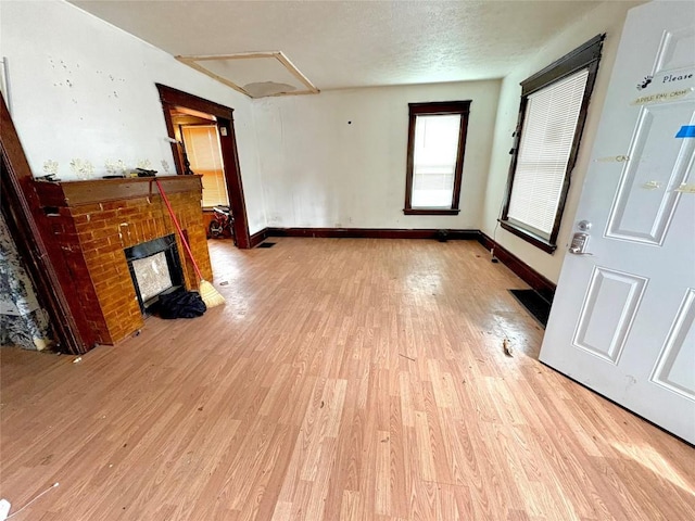 unfurnished living room featuring light wood-style flooring, a fireplace, baseboards, and a textured ceiling