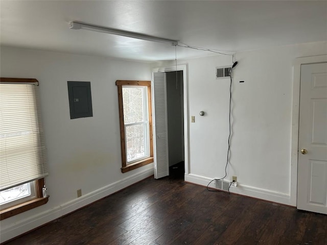 spare room featuring dark wood-type flooring, electric panel, visible vents, and baseboards