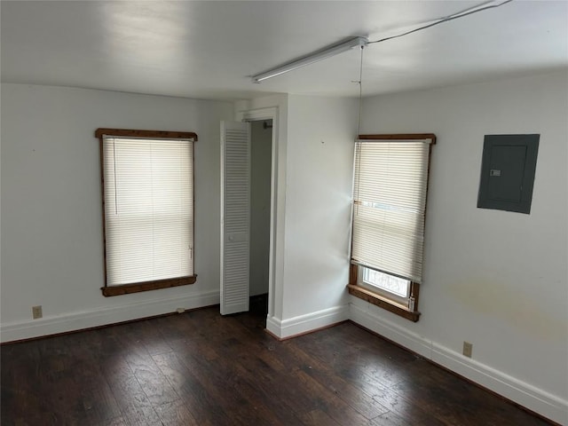 empty room featuring electric panel, baseboards, and dark wood-style flooring