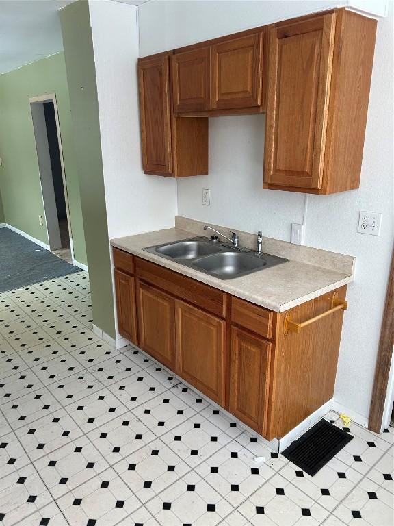 kitchen featuring brown cabinetry, light countertops, a sink, and baseboards