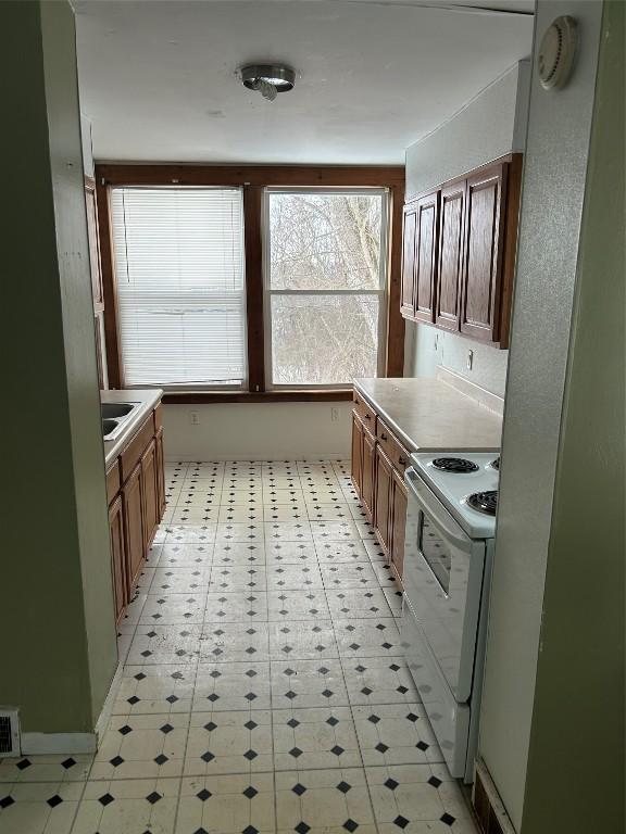 kitchen featuring brown cabinets, light floors, white electric stove, and light countertops