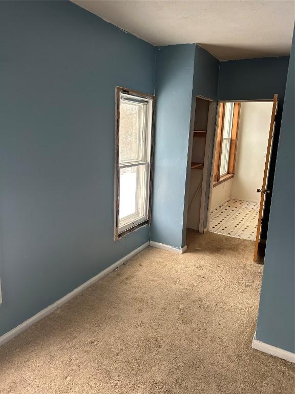 spare room featuring light colored carpet and baseboards