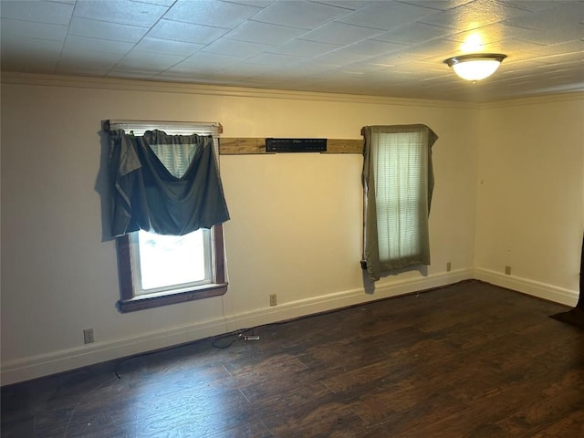 empty room featuring dark wood-style floors, ornamental molding, and baseboards