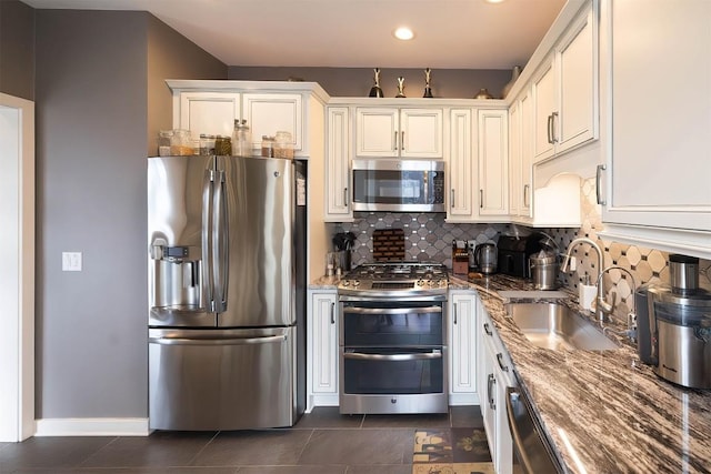 kitchen with stainless steel appliances, a sink, white cabinetry, decorative backsplash, and dark stone countertops