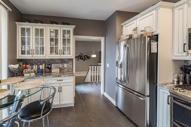 kitchen with light stone counters, stainless steel appliances, backsplash, glass insert cabinets, and white cabinets