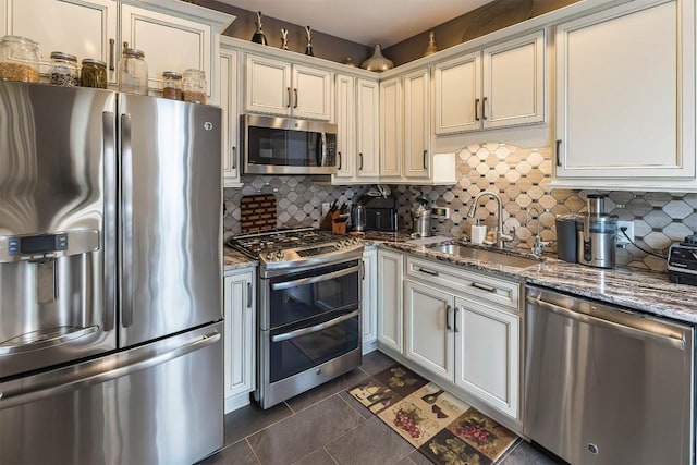 kitchen with appliances with stainless steel finishes, stone countertops, a sink, and backsplash