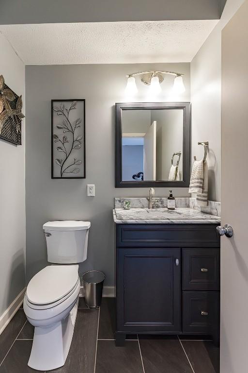 bathroom with baseboards, toilet, tile patterned flooring, a textured ceiling, and vanity