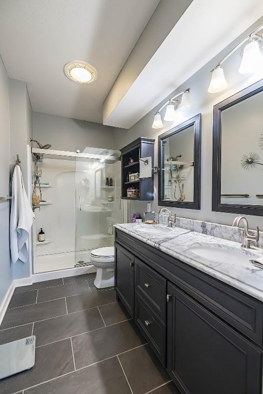 full bathroom featuring a sink, a shower stall, toilet, and double vanity