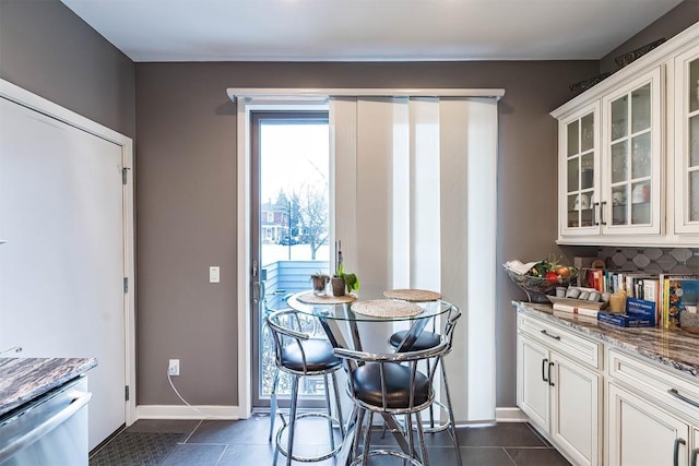 kitchen featuring light stone counters, dark tile patterned flooring, white cabinetry, and decorative backsplash