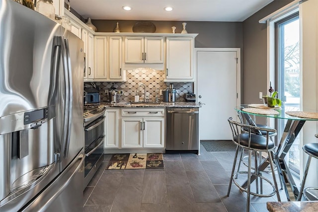 kitchen featuring dark stone countertops, a sink, stainless steel appliances, backsplash, and recessed lighting