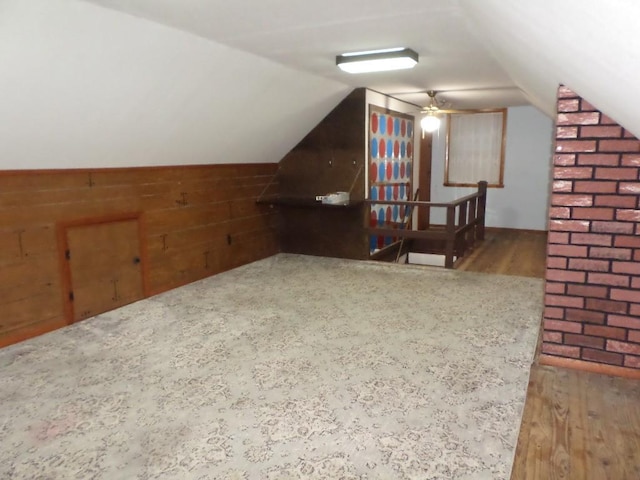 additional living space with wood-type flooring, lofted ceiling, and wooden walls