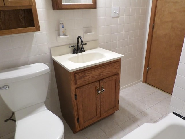 bathroom with tile walls, vanity, toilet, and a tub to relax in