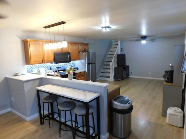 kitchen featuring appliances with stainless steel finishes, a breakfast bar area, light countertops, a peninsula, and light wood finished floors