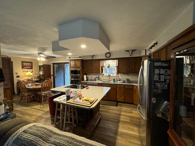 kitchen featuring a kitchen breakfast bar, hardwood / wood-style flooring, ceiling fan, an island with sink, and appliances with stainless steel finishes