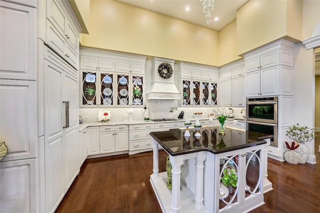 kitchen with a kitchen bar, stainless steel double oven, a kitchen island, dark stone countertops, and white cabinetry