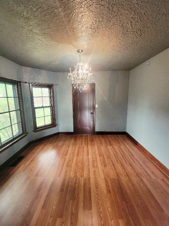 unfurnished room featuring light wood-type flooring, a textured ceiling, and an inviting chandelier