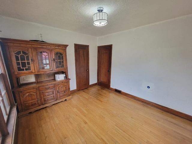 unfurnished dining area with light wood-type flooring and a textured ceiling