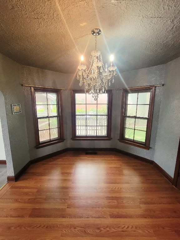 unfurnished dining area featuring a textured ceiling, a notable chandelier, and dark wood-type flooring