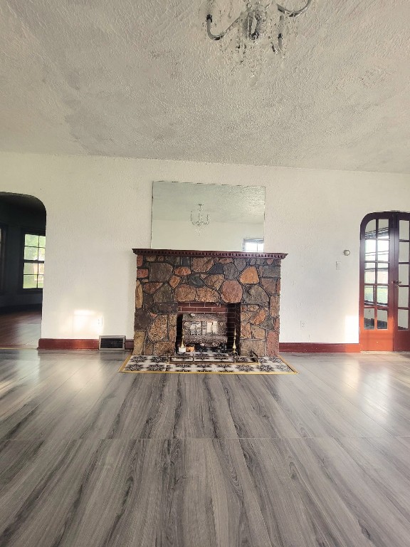 unfurnished living room with a stone fireplace, french doors, hardwood / wood-style floors, and a textured ceiling