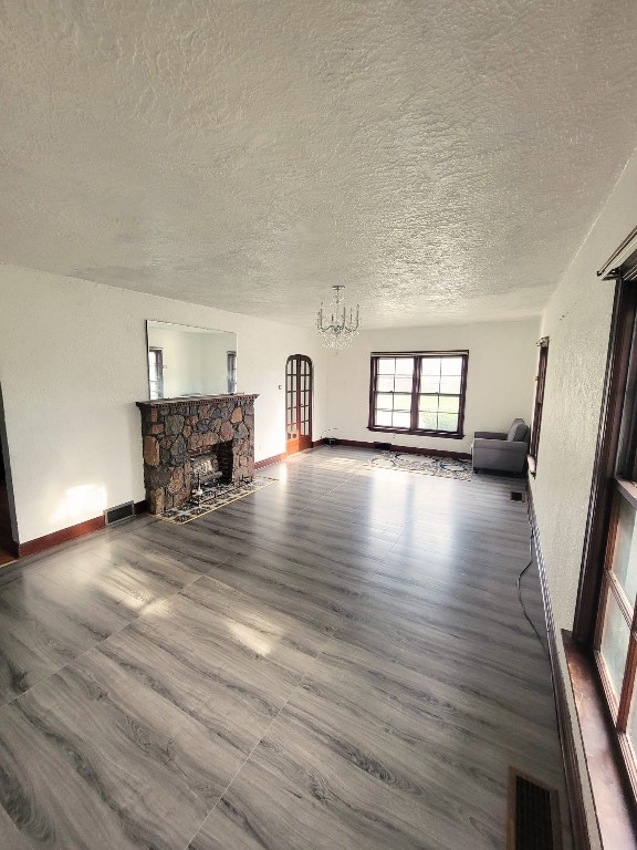 unfurnished living room with a stone fireplace, a textured ceiling, and an inviting chandelier