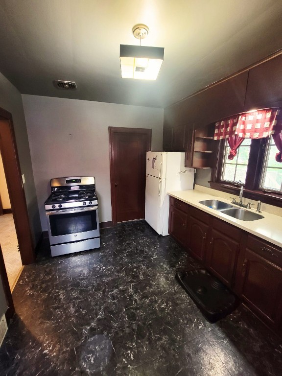 kitchen featuring dark brown cabinetry, sink, white refrigerator, and stainless steel range with gas stovetop