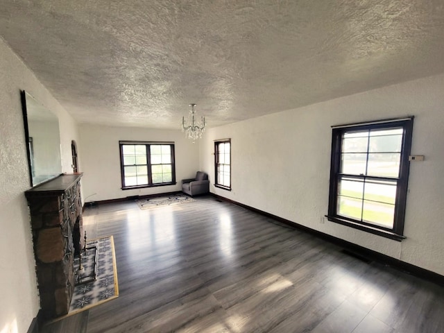 unfurnished living room featuring a stone fireplace, dark wood-type flooring, and a chandelier