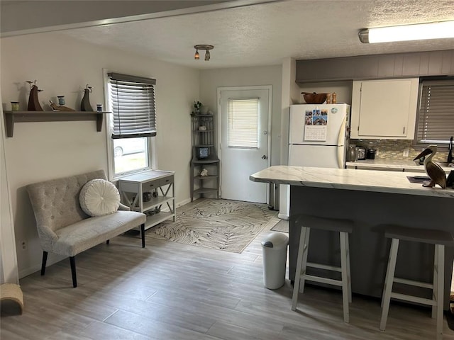 315 Wallace Ave, Linesville, PA 16424 - kitchen with a breakfast bar area, white cabinets, light wood-style flooring, baseboards, and a textured ceiling