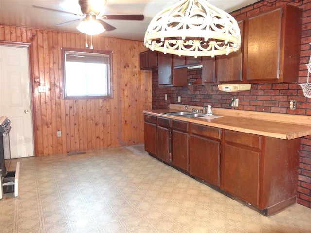 kitchen featuring wooden counters, sink, wooden walls, ceiling fan, and decorative light fixtures