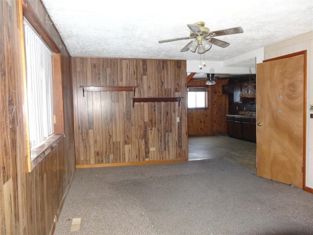 unfurnished living room with carpet flooring, a textured ceiling, ceiling fan, and wood walls