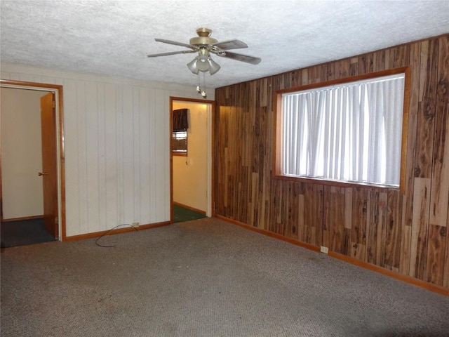 carpeted empty room with ceiling fan, wood walls, and a textured ceiling