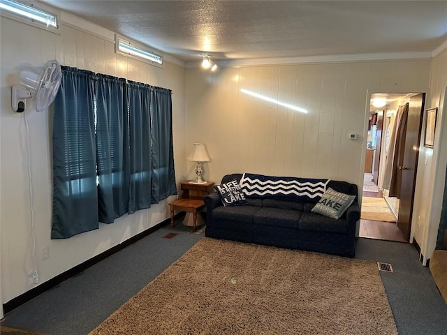 living room featuring carpet flooring, wood walls, ornamental molding, and a textured ceiling